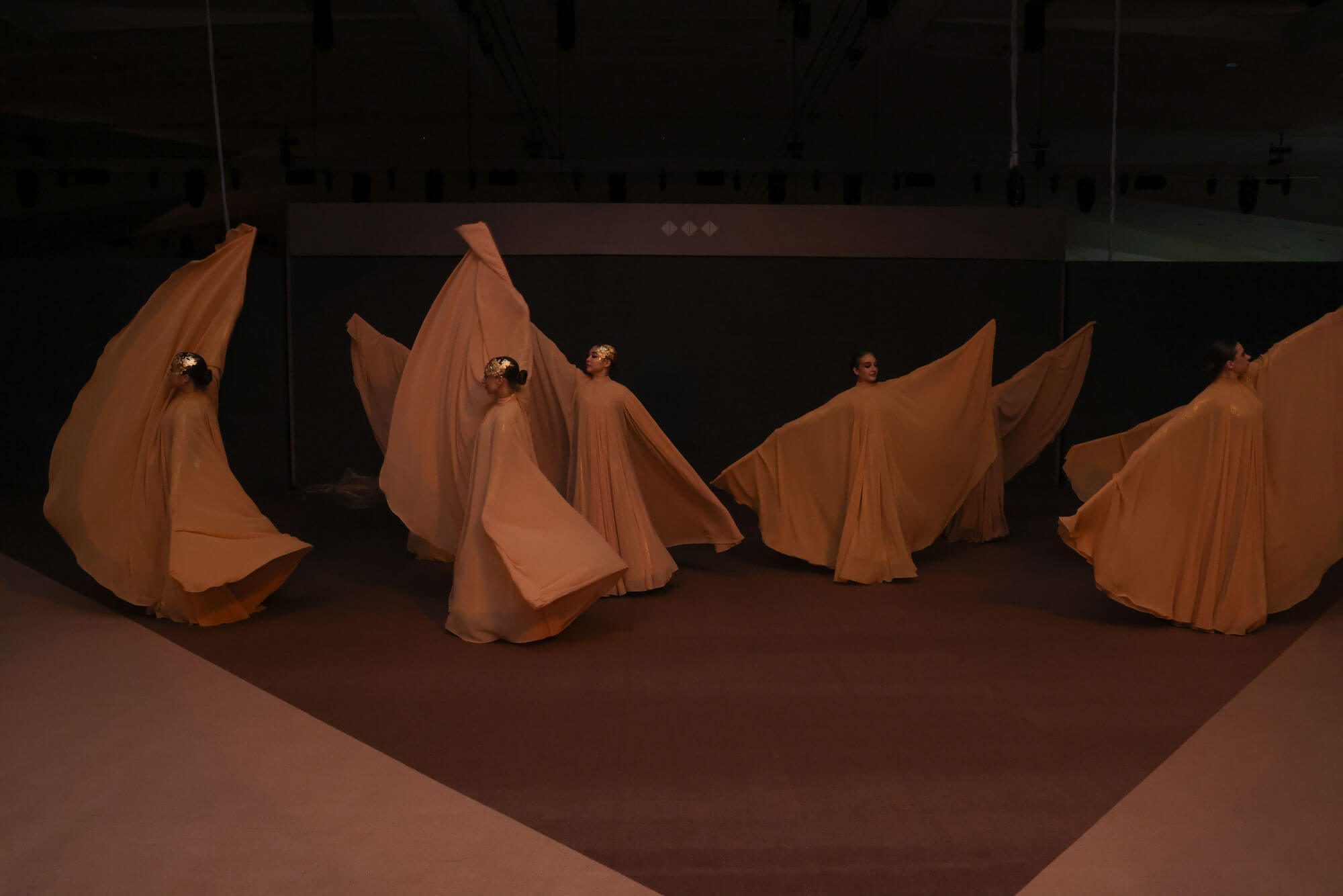 Contemporary dancers performing a choreographed routine with flowing fabric costumes in a dimly lit stage setting