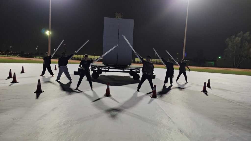 Performers rehearsing with illuminated props in an outdoor stadium setting at night