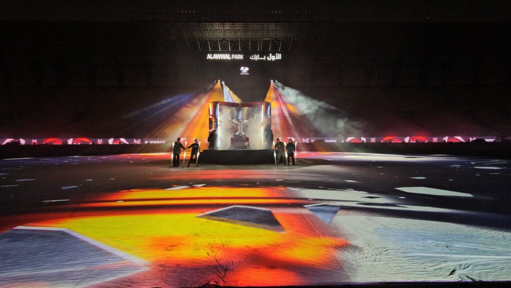 Stadium stage with central trophy display, warm lighting, and floor projections during a live ceremony