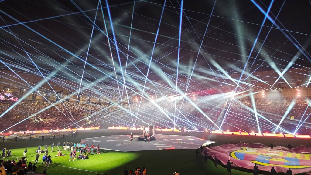 Large-scale stadium show with laser lighting, performers, and crowd during a live event