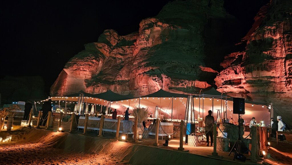 Outdoor desert event setup with illuminated rock formations and a tented dining experience at night