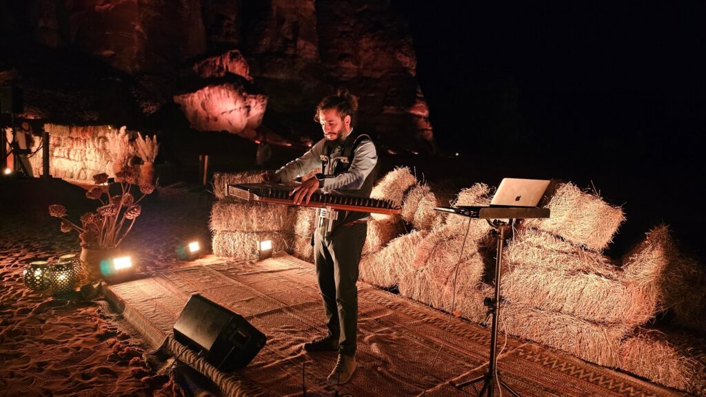 Musician performing on a traditional string instrument at a desert event with warm ambient lighting