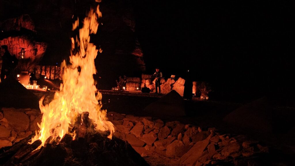 Fire pit lighting an outdoor desert event with live musician performing in the background at night