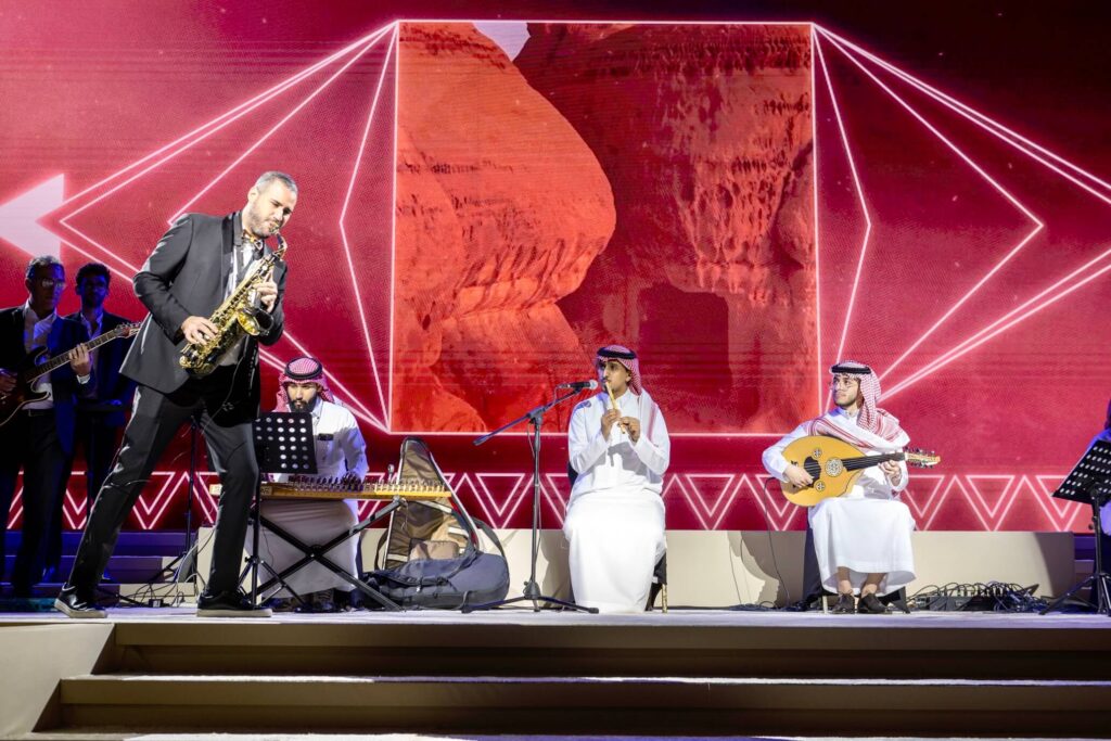 Live music performance featuring saxophonist and traditional Saudi musicians on stage with immersive visual backdrop